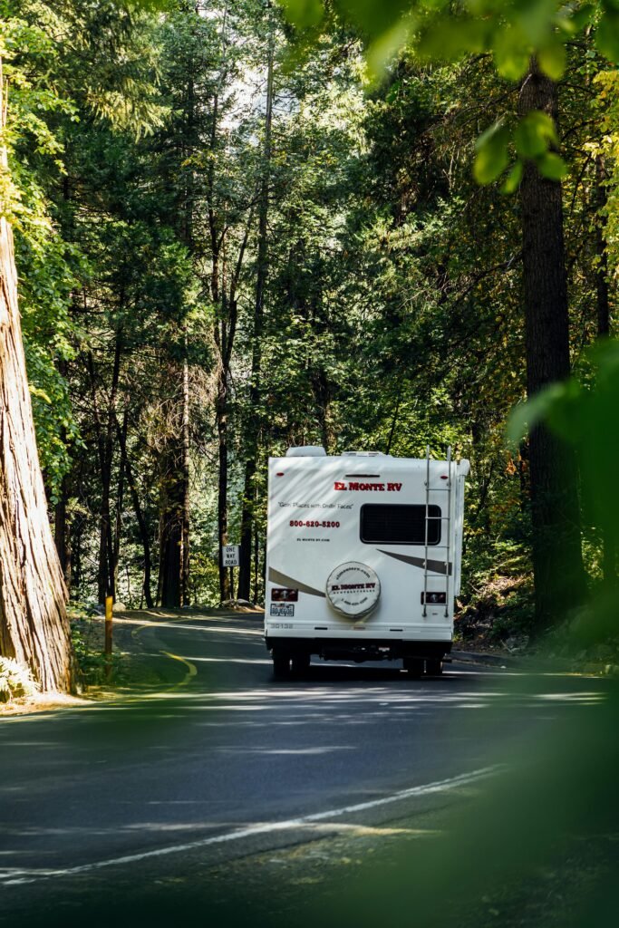 White RV traveling through lush forest on a winding mountain road.