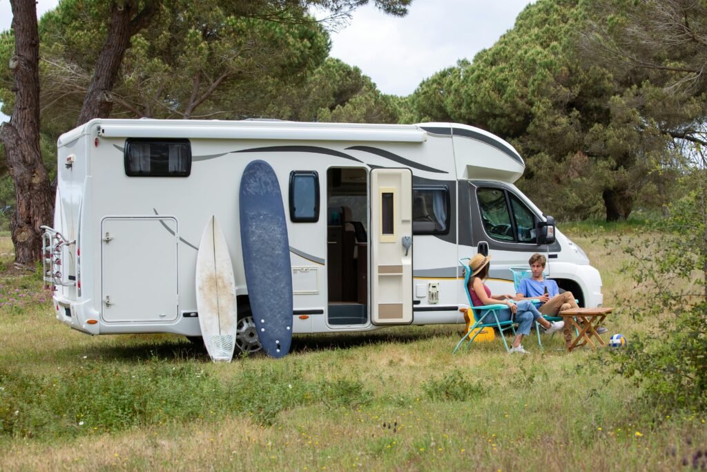 A couple relaxes outside their RV with surfboards at a scenic campsite in Portugal, enjoying a summer vacation.