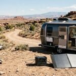 A Starlink satellite dish on the ground connected to an ALLPOWERS portable solar generator and a foldable solar panel next to an Airstream travel trailer parked off-grid in a desert landscape.