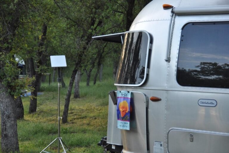 Class C motorhome parked at an outdoor campsite with a satellite dish antenna setup on top