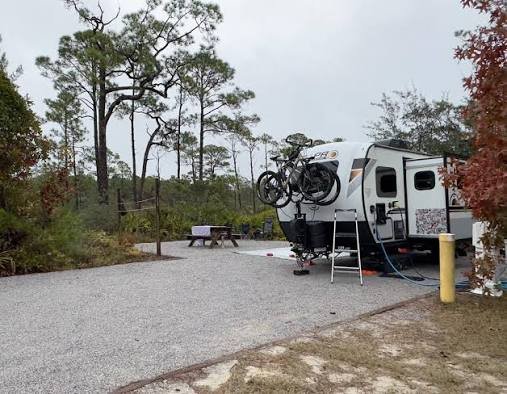 Class A motorhome parked at a paved campsite surrounded by pine trees at Grayton Beach State Park, Florida